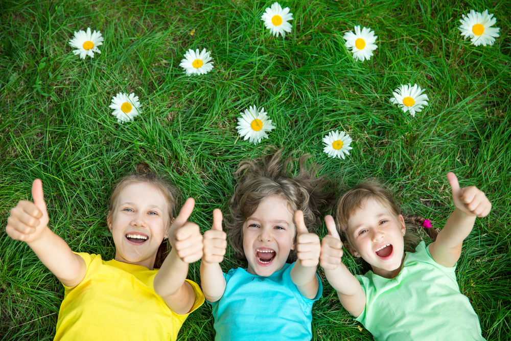 Akademia JA - Trzy małe dziewczynki leżące na trawie z kciukami do góry podczas treningu interpersonalnego Gdańsk.